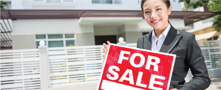 real estate agent holding a for sale sign outside of a home