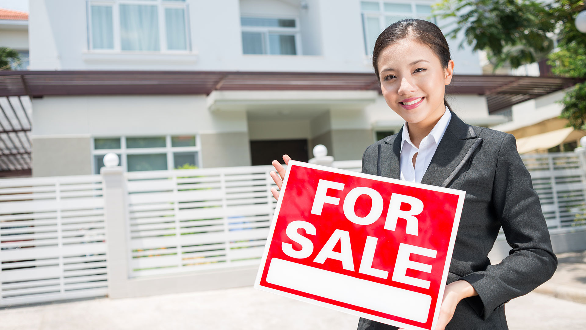 real estate agent holding a for sale sign outside of a home