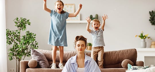 mother meditating while two children jump on the couch