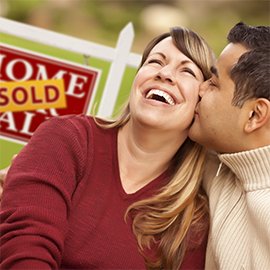 husband and wife sitting in front of a sold home sign