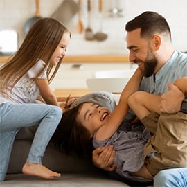 father playing with his two children on the couch